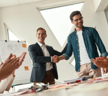 New team member. Two cheerful colleagues shaking hands and smiling while having a meeting in the