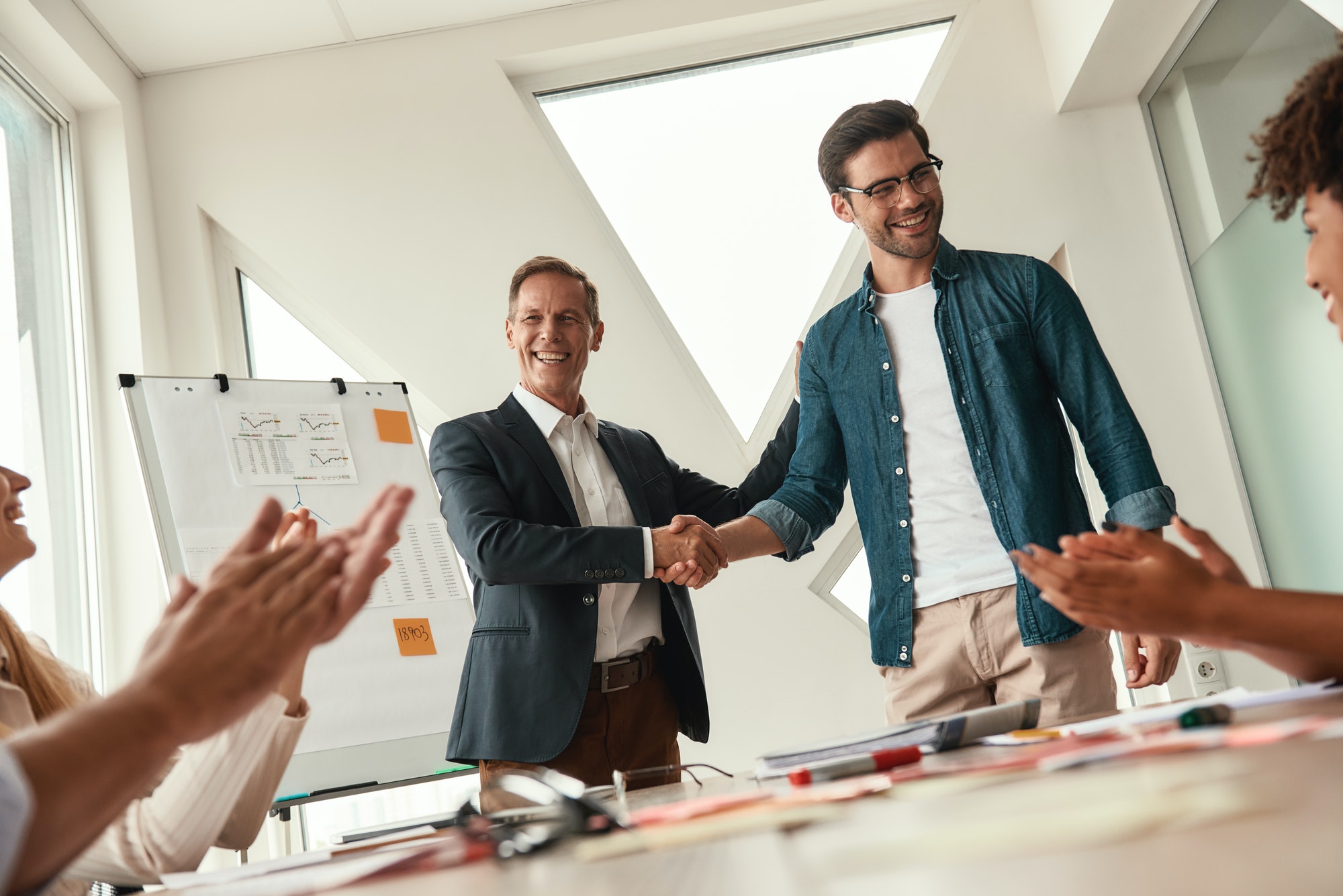 New team member. Two cheerful colleagues shaking hands and smiling while having a meeting in the